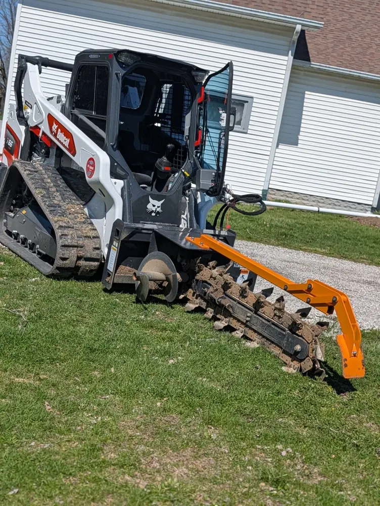 Busy Man Contracting Bobcat loader using a stump grinding attachment beside a residential driveway