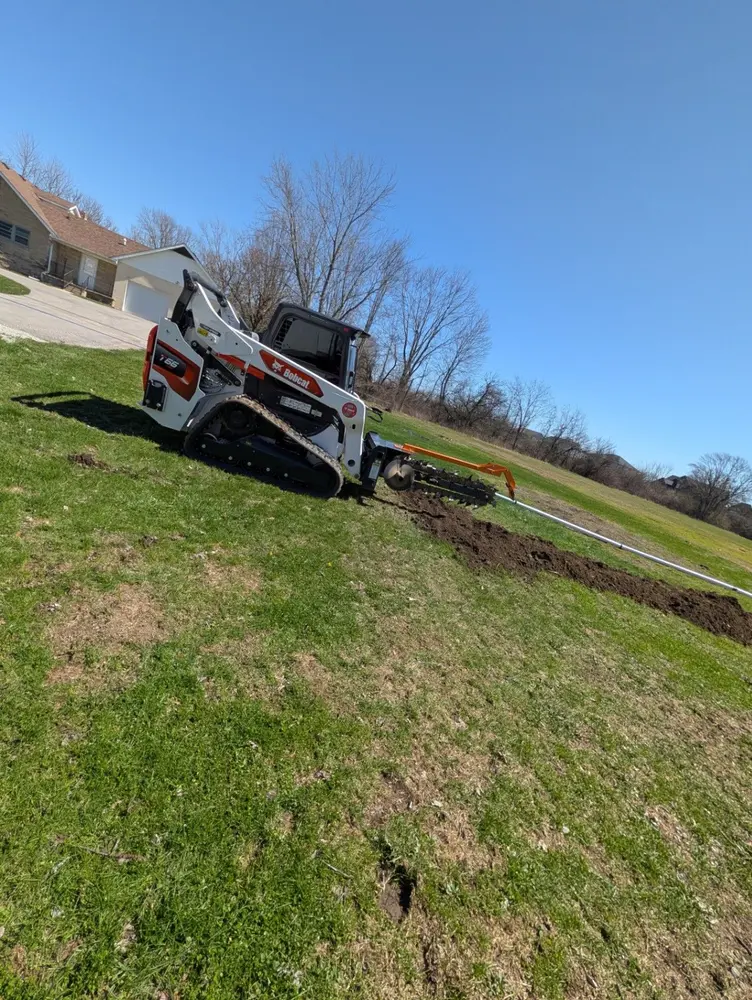Bobcat loader carefully positioned on a grassy slope near a home